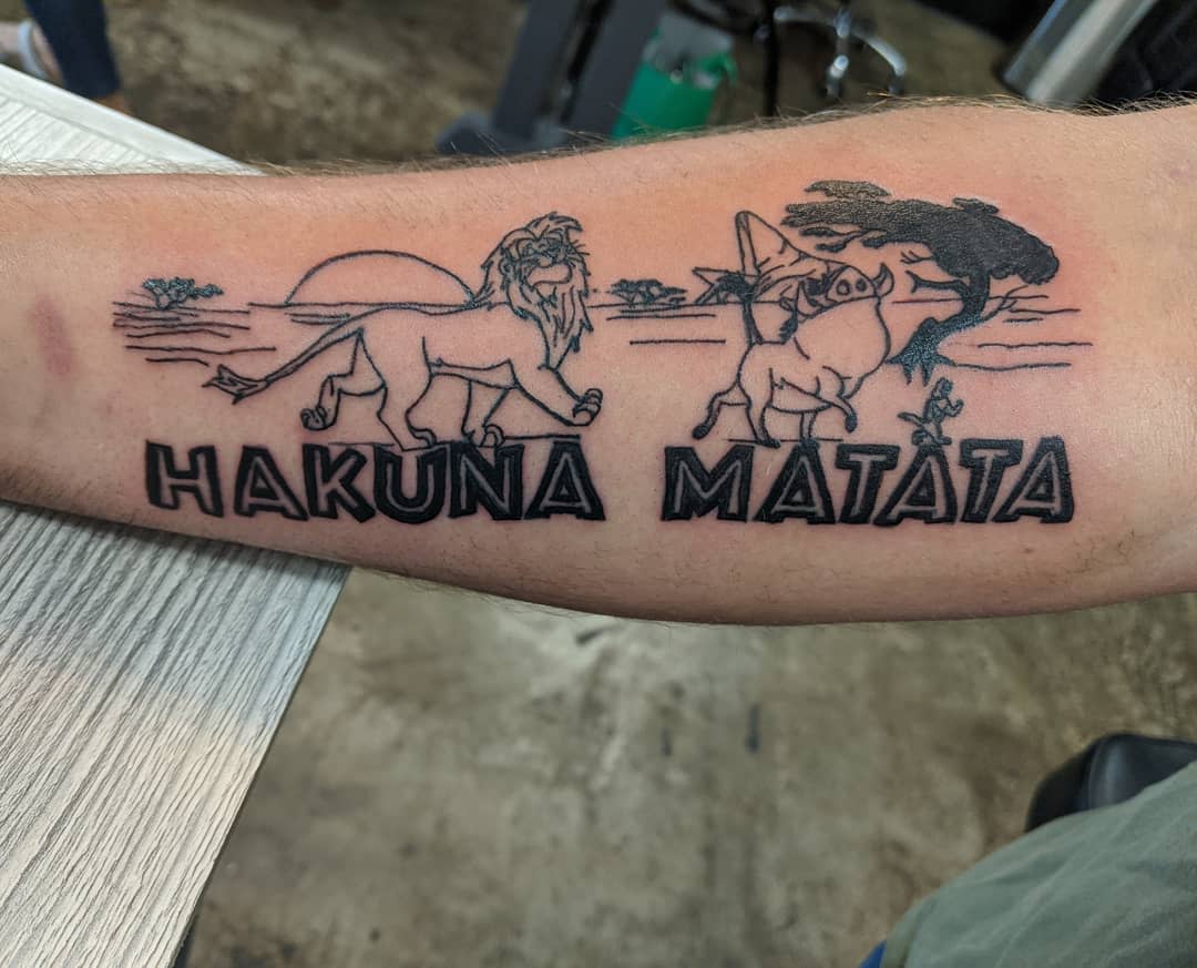 Tattoo of "Hakuna Matata" with characters from The Lion King on a forearm